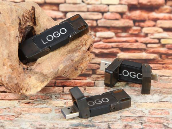 USB-Sticks in schwarzem Gehäuse mit Platz für individuelle Logos, dekorativ auf Holz und Stein präsentiert.