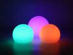 Bunte LED-Leuchtmittel in Kugel-Form, leuchtend in Grün, Violett und Orange, auf dunklem Hintergrund.