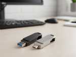 Zwei elegante USB-Sticks in Schwarz und Silber auf einem Schreibtisch, ideal für individuelles Branding und Datenspeicherung.