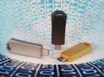 Drei verschiedene USB-Sticks in Silber, Schwarz und Gold auf einem binären Hintergrund, ideal für individuelle Werbeanwendungen.