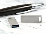 USB-Stick in modernem, silbernem Design mit Platz für individuelles Branding und einem stylischen Kugelschreiber im Hintergrund.