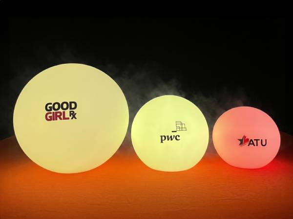 Drei leuchtende Kugeln in verschiedenen Größen mit aufgedruckten Logos von GOOD GIRL, pwc und ATU.