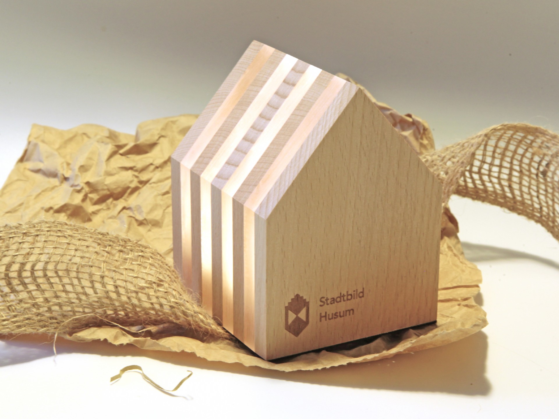 Holzfigur in Form eines Hauses mit durchscheinenden Lamellen und bedrucktem Logo 