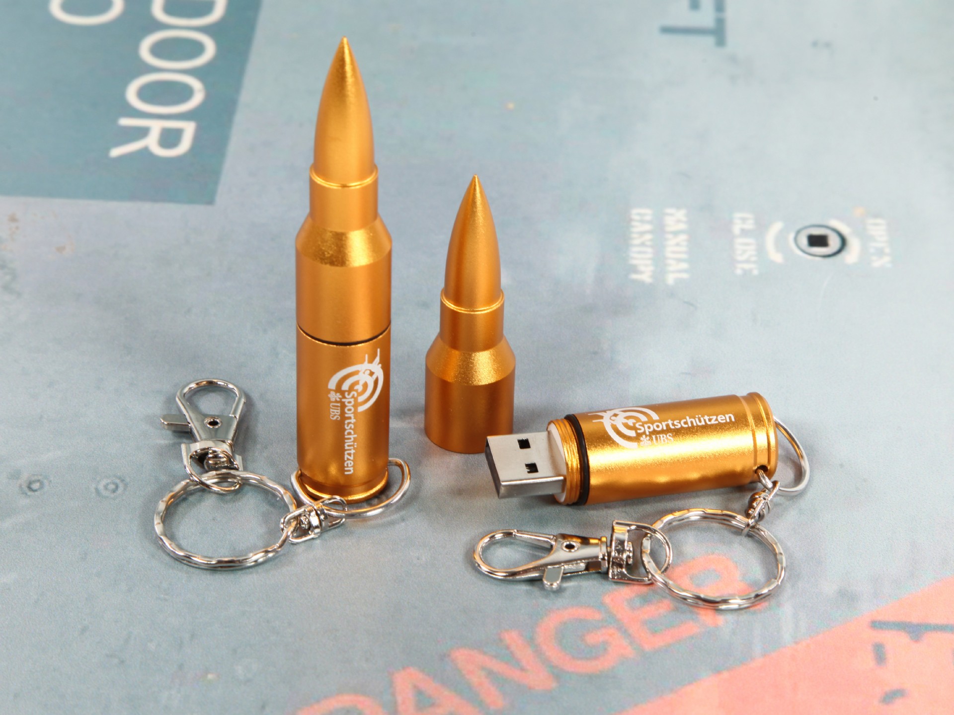 USB-Stick in Form einer Patronen mit goldenem Gehäuse und Schlüsselanhänger, ideal für individuelle Werbeartikel.